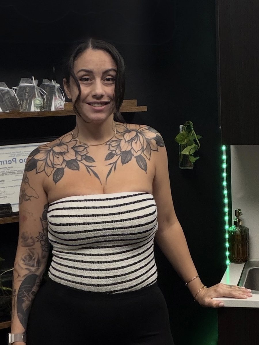 Davi in her Pretty Ugly studio in Charlotte, floral chest and sleeve tattoos, standing by the counter