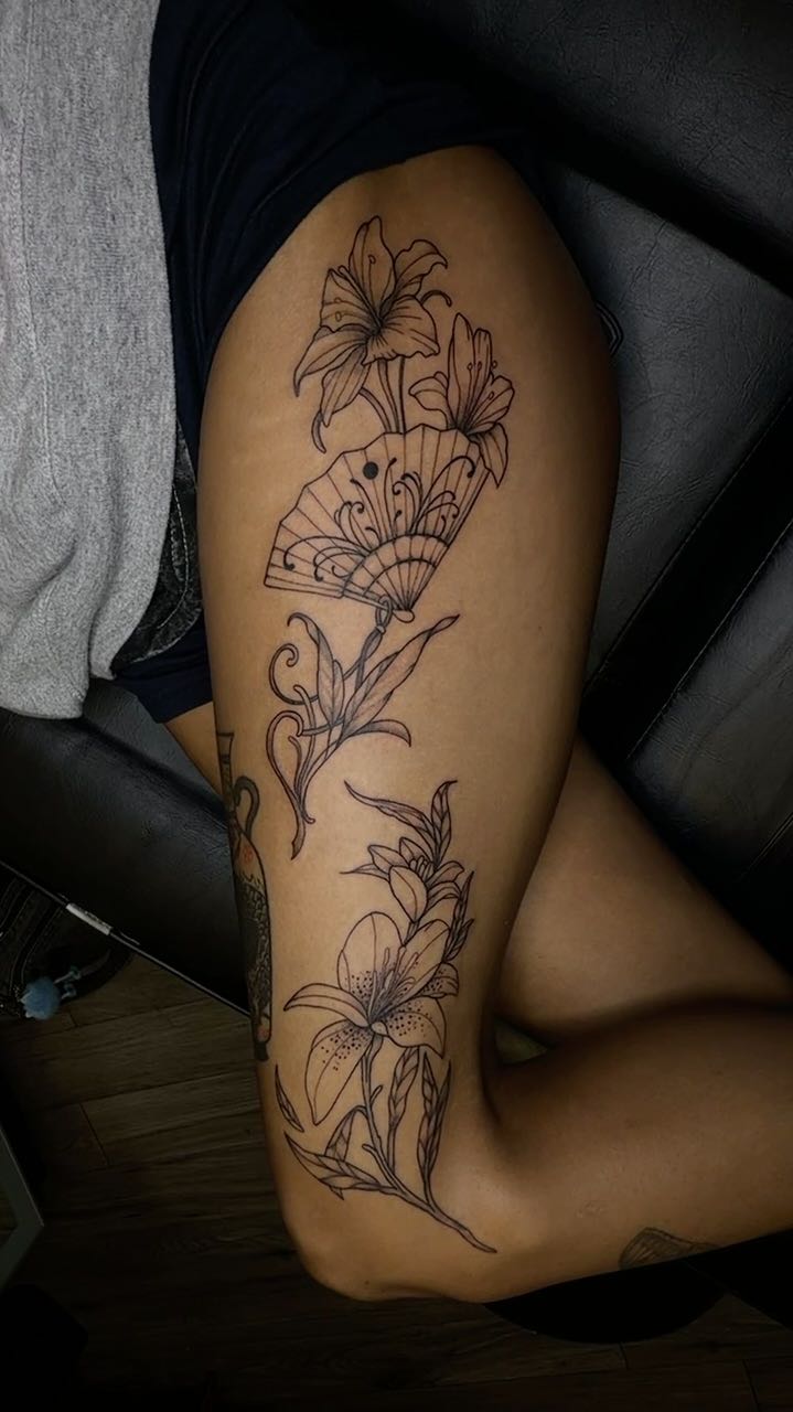 Fine-line floral tattoo with a fan, on a client's thigh
